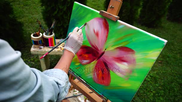 Hand van vrouwen kunstenaar leidt borstel op groene achtergrond op Canvas en gemengde kleuren tegen de achtergrond van groen gras en Bench met Art Tools Outdoors. - Video