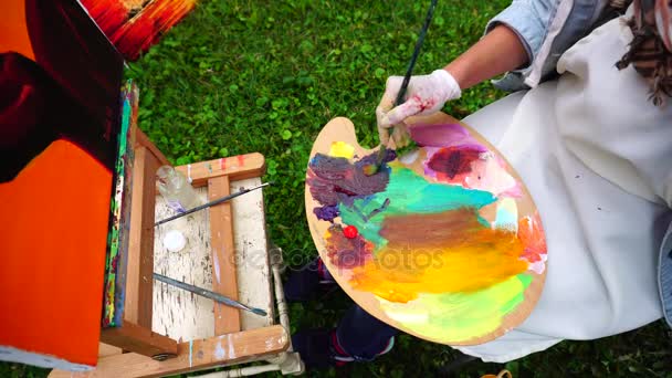 Vrouwelijke schilder Hand mixen kleuren om gewenste tint naar de Paint-afbeelding en zit op stoel achter ezel buiten buiten in Park. - Video