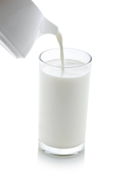 Γάλα που ρίχνει από μια κανάτα σε ένα ποτήρι σε λευκό φόντο - Φωτογραφία, εικόνα