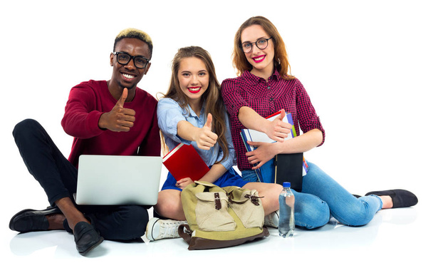 Tres estudiantes felices con libros, laptop y bolsos con pulgares arriba
 - Foto, imagen