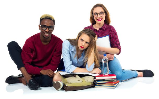 drei glückliche Studenten sitzen mit Büchern, Laptop und Taschen - Foto, Bild