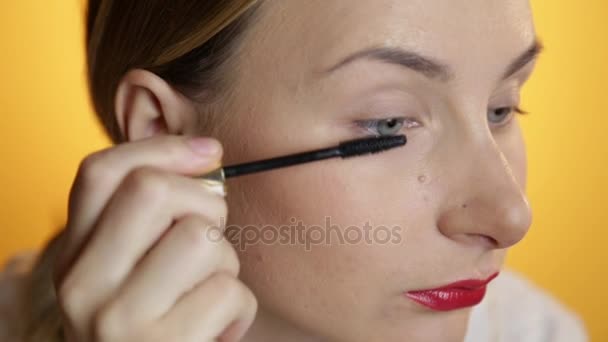 Beautiful happy young lady putting makeup on a yellow background - Filmati, video