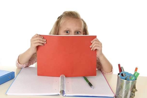 schoolmeisje met blond haar lachend gelukkig zittend op Bureau speelse terwijl het doen van huiswerk - Foto, afbeelding