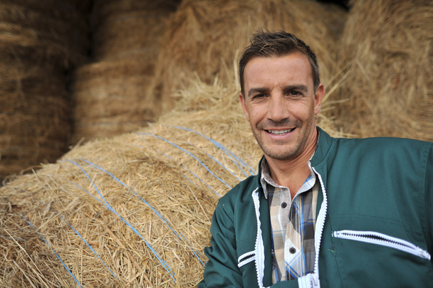 Portrait of cheerful farmer standing in front of hay rolls - Fotoğraf, Görsel