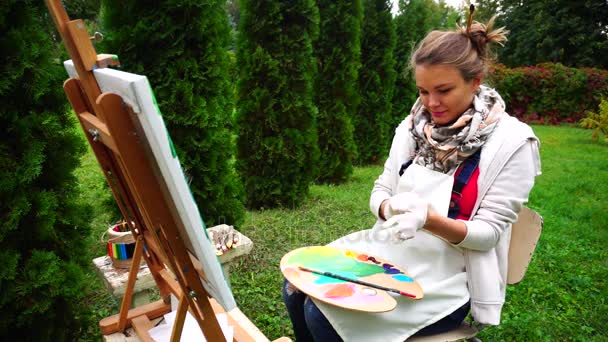 女性の繊細な画家の手にグローブを着用してカメラに笑みを浮かべて、屋外の公園で座っています。. - 映像、動画