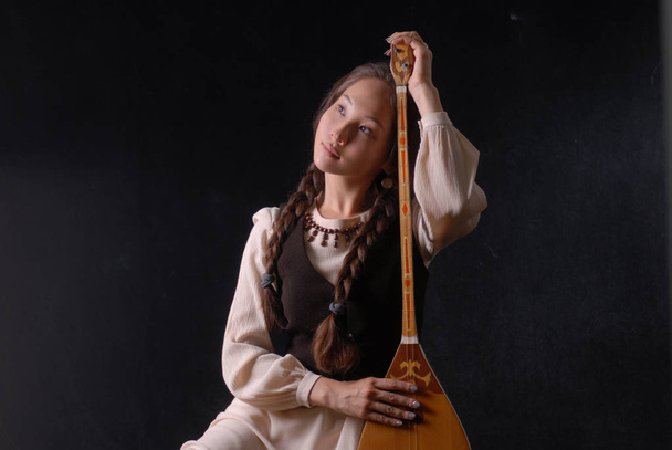 Joven asiática modelo en nacional vestido sentado con kyrgyz komuz
 - Foto, imagen
