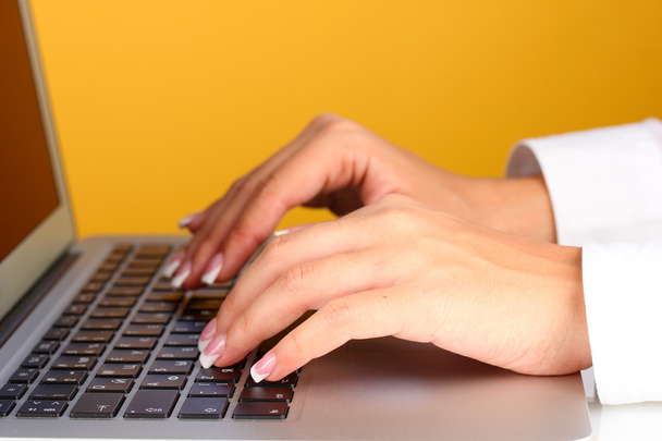 Hands typing on laptop keyboard close up on orange background - Valokuva, kuva