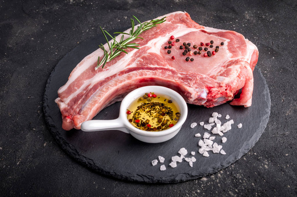 Nyers hús, a sötét háttér előtt. Nyers sertés steak gyógynövények, olajból és fűszerekből állnak. Főzés hús - Fotó, kép