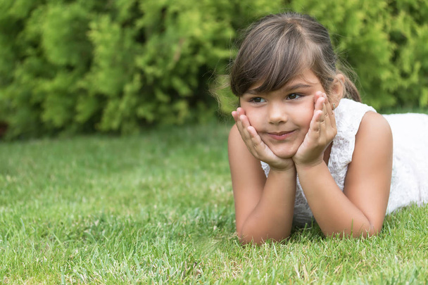 Cool brunette little girl lying on the grass  - Fotoğraf, Görsel