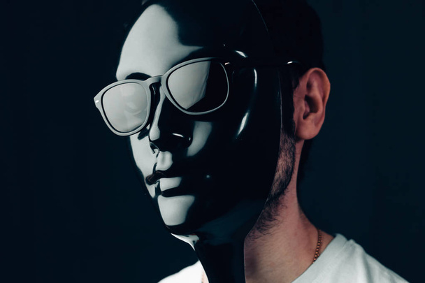 Ο άνθρωπος στη μαύρη γυαλιστερή μάσκα και γυαλιά ηλίου. Studio οριζόντια πορτρέτο σε γκρο πλαν. - Φωτογραφία, εικόνα