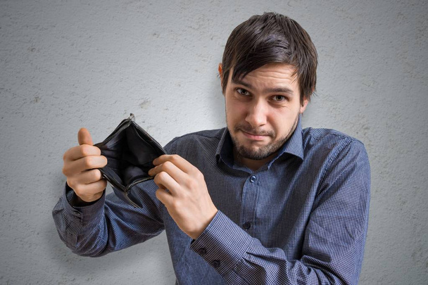 破産や倒産の概念。若い男はお金を持たず、空の財布を見せています。. - 写真・画像