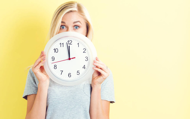  Woman holding clock showing nearly 12 - 写真・画像