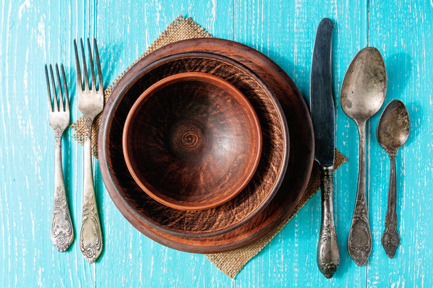 Коричневі тарілки з столовими приборами на сільському дерев'яному столі, вид зверху
 - Фото, зображення