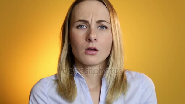 A cute young white woman makes a sad face on a yellow background - Video