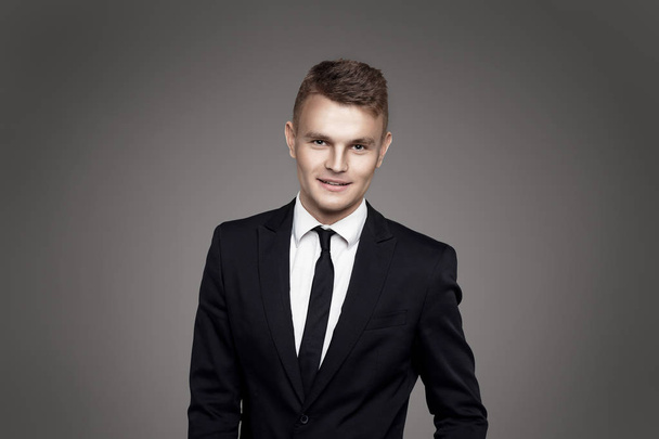Young trendy man. Black suite and tie, gray background. Portrait - Photo, Image