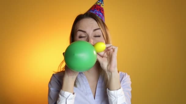 Beautiful girl blowing balloons on a yellow background - Кадры, видео