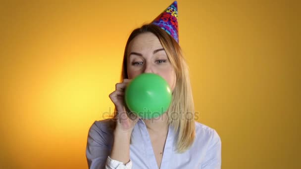 Beautiful girl blowing balloons on a yellow background - Imágenes, Vídeo