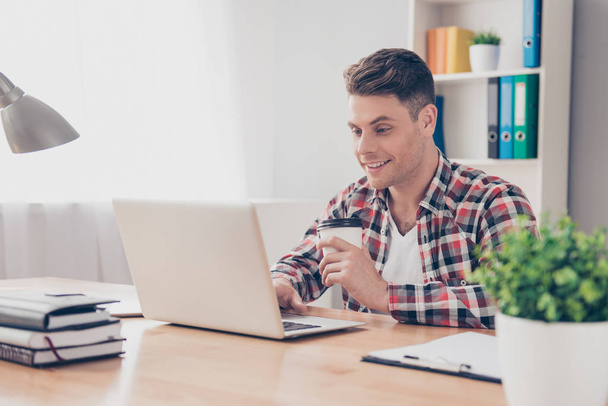 Young happy guy with cup of coffee using laptop - Photo, image