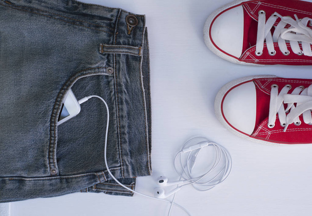 Голубые джинсы с мобильным телефоном в кармане рядом с молодежной красной обуви
 - Фото, изображение