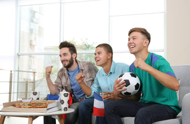 Futbolistas con pizza viendo el juego en la habitación
 - Foto, imagen