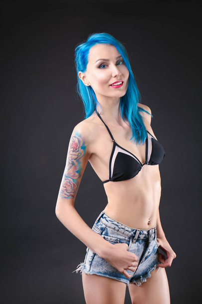 Kaunis nuori nainen, jolla on tyylikäs väri hiukset ja tatuointi tummalla taustalla
 - Valokuva, kuva
