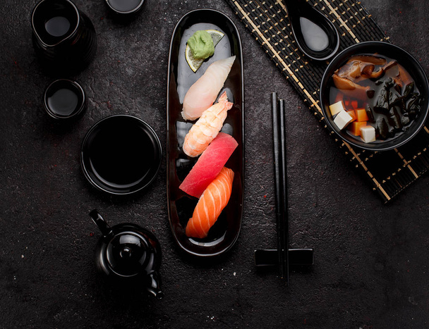 Sushi set on a black plate and miso soup over dark concrete background - Photo, Image