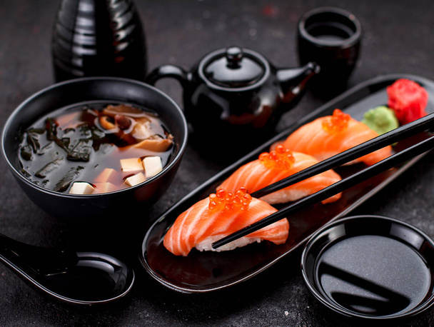 Japanese cuisine. Salmon sushi nigiri and miso soup on black plate a dark table. - Фото, зображення