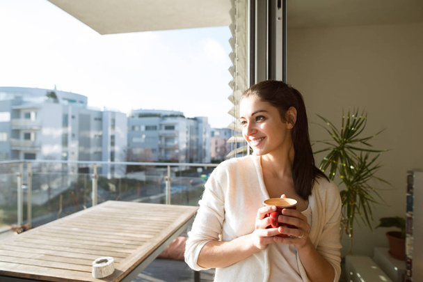 Woman relaxing on balcony holding cup of coffee or tea - Фото, зображення