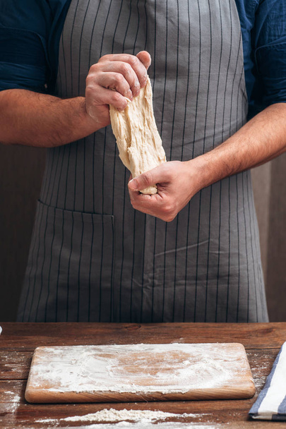 Unrecognizable baker stretching dough at kitchen - Zdjęcie, obraz