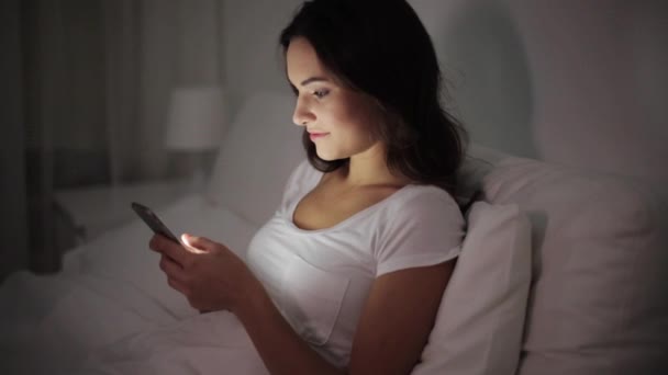 happy young woman with smartphone in bed at night - Video, Çekim