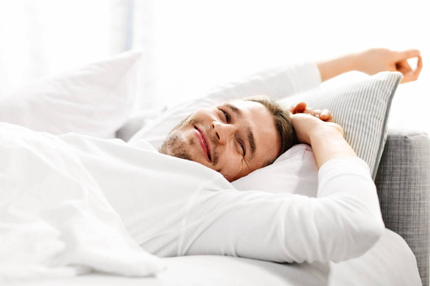 Pohledný muž táhnoucí se v posteli - Fotografie, Obrázek