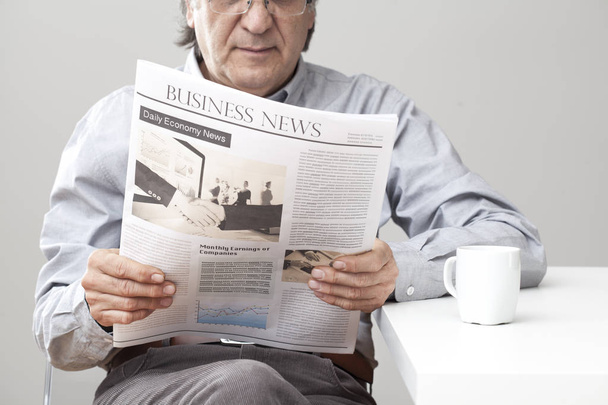 Homem sênior lendo jornal em fundo cinza
 - Foto, Imagem
