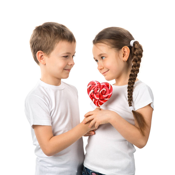 Junge schenkt einem kleinen Mädchen Süßigkeiten roten Lutscher in Herzform isoliert auf weiß. Valentinstag. Kinder lieben. - Foto, Bild