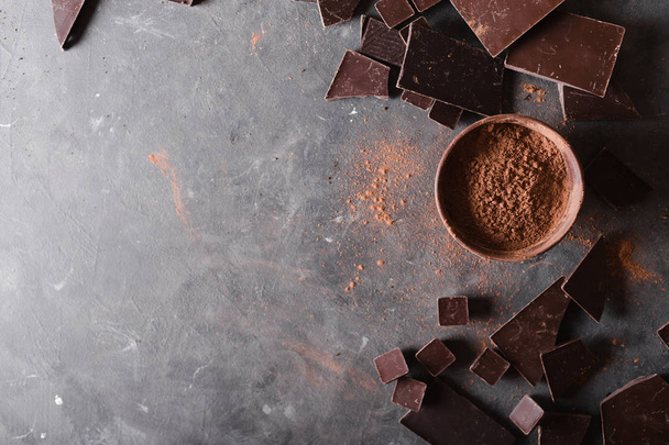 Chocolate  chunks and cocoa powder. Chocolate bar pieces.  A large bar of chocolate on gray abstract background. Background with chocolate. Slices of chocolate, - Zdjęcie, obraz