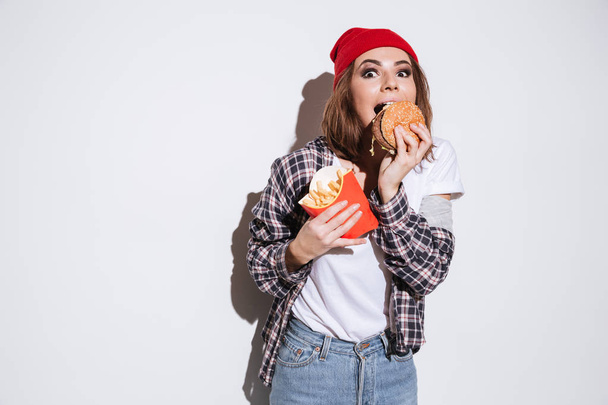 Hungry young woman eating fries and burger - Foto, imagen