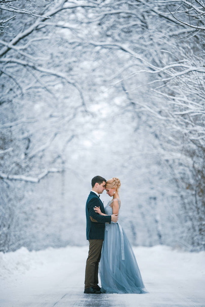 Noiva e noivo entre estrada nevada na floresta
. - Foto, Imagem