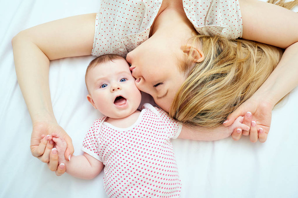 Мама целует ребенка, лежащего на кровати крупным планом
 - Фото, изображение