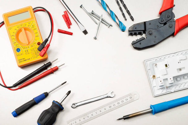 Various electrician tools and components including a multimeter, screwdrivers, wirecutters, drill bits, switches and sockets. - Photo, Image