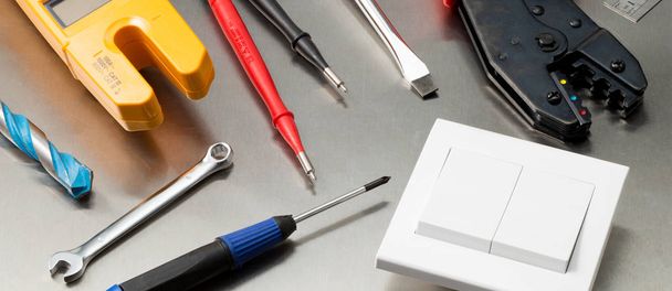Various electrician tools and components including a multimeter, screwdrivers, wirecutters, drill bits, switches and sockets. Web banner format. - Photo, Image