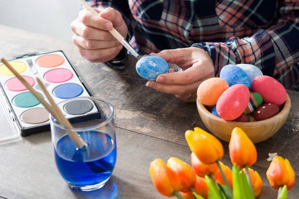 Женщина рисует пасхальные яйца на деревянном столе
 - Фото, изображение