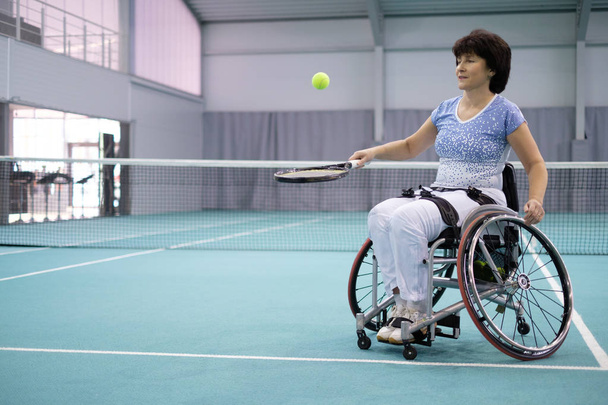 Femme mature handicapée en fauteuil roulant jouant au tennis sur un court de tennis
 - Photo, image