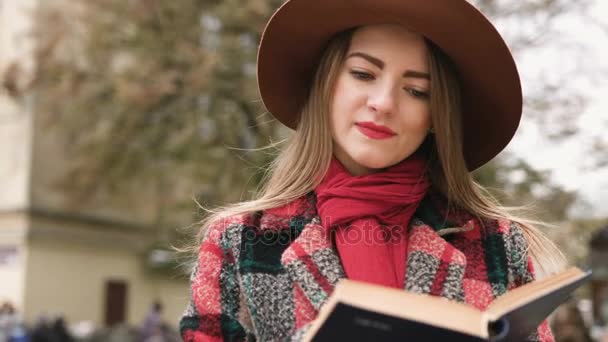 Молода красива дівчина в капелюсі читає книгу в міському парку. Повільний рух
. - Кадри, відео