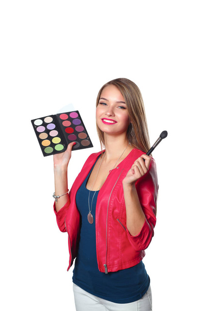 Fiatal gyönyörű nő tartja az egyik kezében, és egy paletta festék és árnyékok smink, használt kefe smink - Fotó, kép