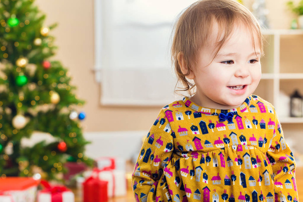 Kleuter meisje glimlachend tegenover een kerstboom - Foto, afbeelding