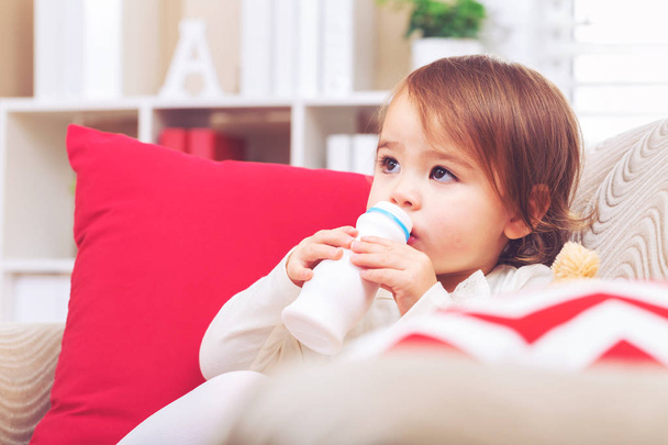 Toddler girl drinking milk in her living room - 写真・画像