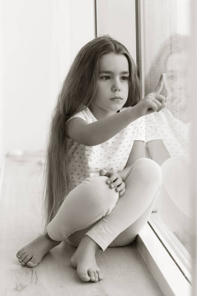 Little sad girl sitting on windowsill - 写真・画像