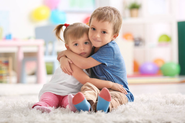 Cute funny children hugging while sitting on carpet at home - Foto, Imagen