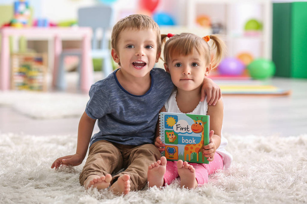 Lindos niños divertidos sentados en la alfombra con libro
 - Foto, imagen
