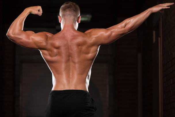 muskulöser Mann lässt Muskeln in Turnhalle spielen - Foto, Bild