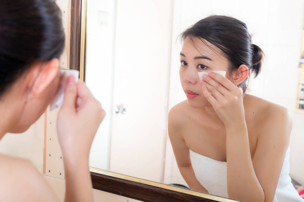 Beautiful woman removing makeup from her face in bathroom. - Foto, Bild